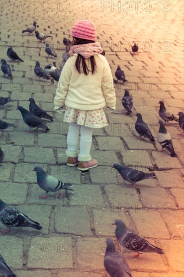 Little girl amid grey pigeons live in large groups in urban environment