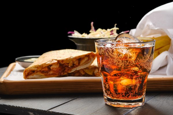 Glass of cola with ice with tortilla and fried potato on background