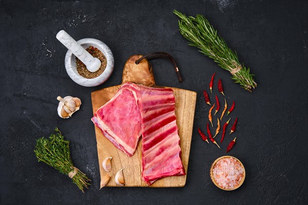 Fresh raw lamb breast ribs on wooden cutting board with herbs and seasoning