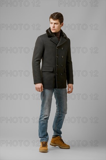 Full length portrait of handsome man in warm woolen coat posing in studio