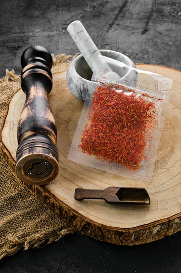 Wooden cross section with saffron in plastic package and stone mortar and mill