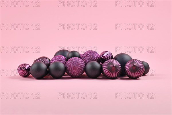 Pile of dark purple and black Christmas tree ornaments in shape of round ball baubles on pink background