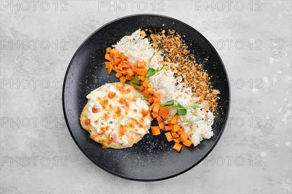 Chopped pork cutlet baked with ham and cheese served with carrot and rice on a plate