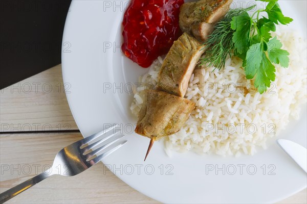 Close up view of plate with pork shaslyk with rice and tomato sauce on wooden table
