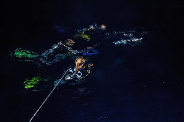 Divers swim at night on boat line line from dive boat sea surface water surface prepare for descent for night dive