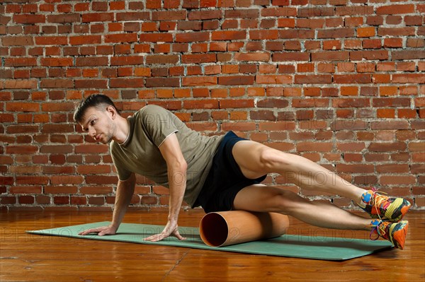 Young male cyclist athlete training and doing workout with barrel on gym mat. Fitness workout