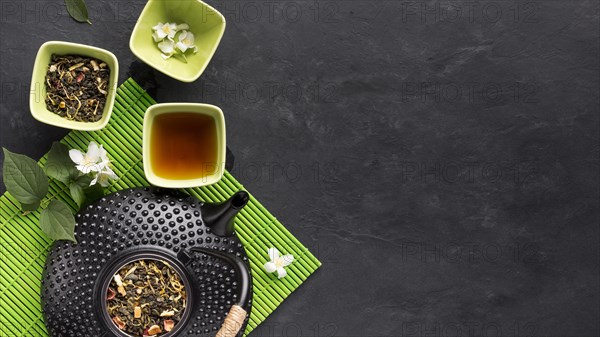 Raw herbal tea ingredient with teapot green placemat black surface