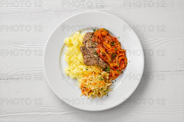 Top view of plate with chopped meat backed with bell pepper with mashed potato and cabbage salad