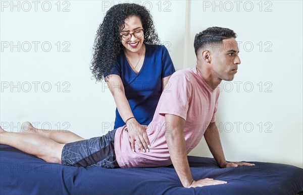 Smiling female physiotherapist with male patient performing lumbar massage treatment. Physiotherapist performing back lumbar rehabilitation to patient