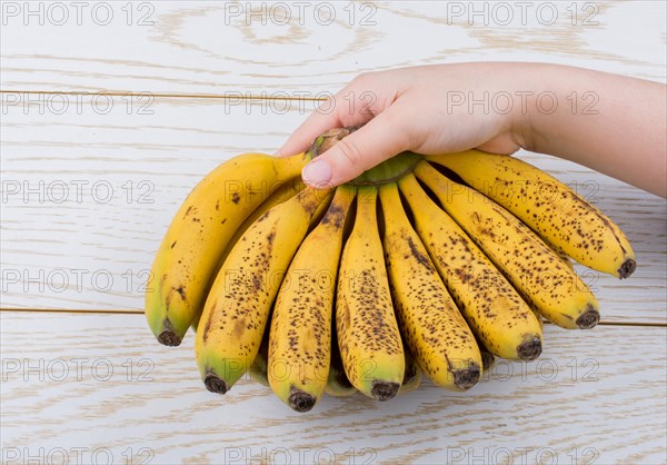 Hand holding bunch of freckled bananas on a wooden texture