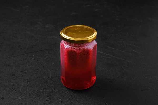 Whole closed jar of cherry jam on black background