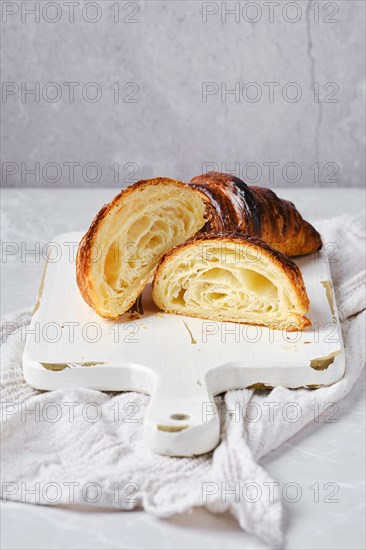 Cross section of classic croissant on bright background and white wooden board