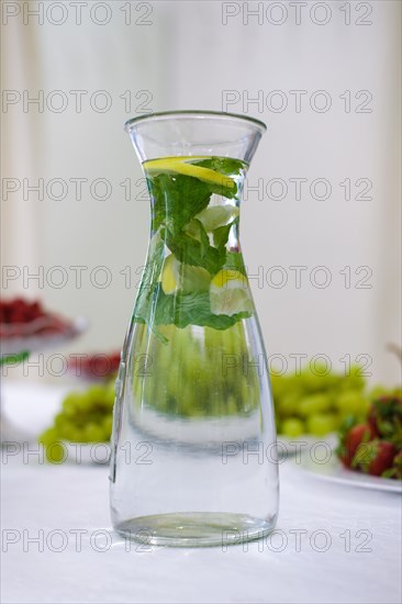 Soft focus photo of decanter with mint and lemon lemonade on table with fruits on bacground