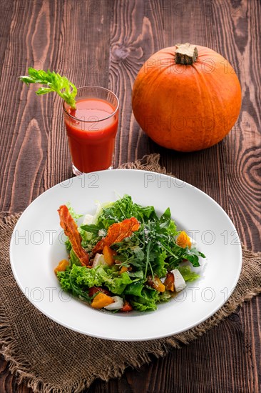 Salad with feta and bacon with tomato juice and pumpkin on wooden table