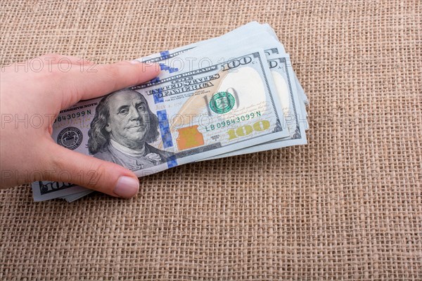 Hand holding banknote bundle of US dollar on a linen canvas background