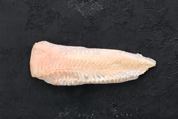 Raw shallow-water hake fillet on black concrete background