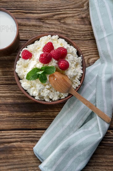 Fresh cottage cheese with raspberries and wooden spoon in clayware on wooden table