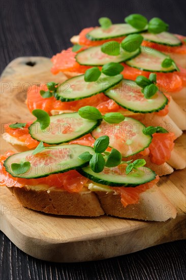 Sandwich with salmon on wooden plate on dark wooden table