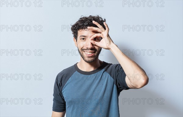 Friendly guy making ok gesture looking through fingers. Happy young man making ok gesture with hand looking through fingers. Teenage guy making ok gesture looking through fingers