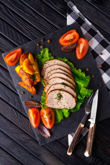 Sliced baked ham with fresh tomatoes on a stone plate in a rustic style