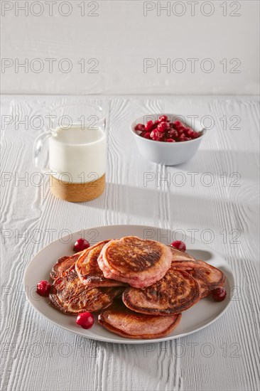 Pancakes with cherry and glass of milk on white kitchen table