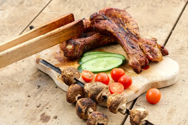 Grilled ribs and champignon on skewer served with fresh cucumber and tomato on wooden table outdoor