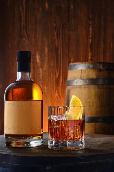 Bottle and glass with blended malt scotch whisky with a barrel on background