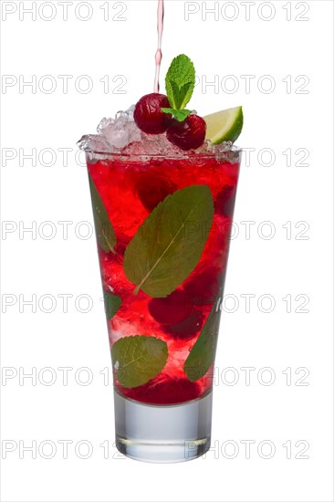 Pouring cherry juice to alcoholic cocktail with lime and mint isolated on white