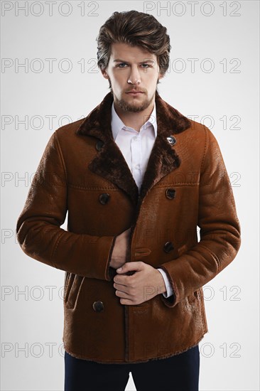 Brutal handsome unshaven man with beard and moustache in sheepskin coat with fur collar