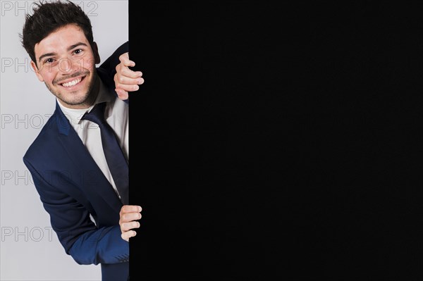 Smiling young businessman peeking from black placard. Resolution and high quality beautiful photo