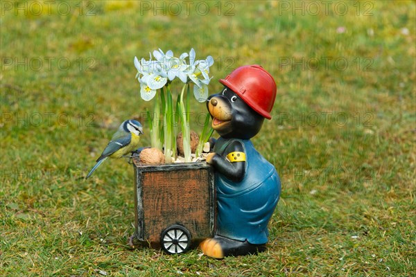 Blue Tit on Mole Figure with Flower Stick Sitting in Green Grass Looking Right