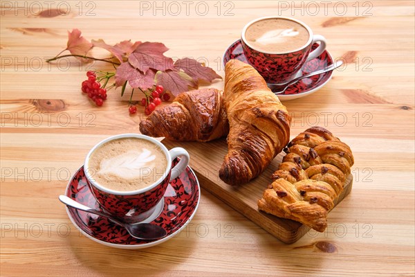 Puff pastry raisin bun and crispy croissant on wooden table with coffee