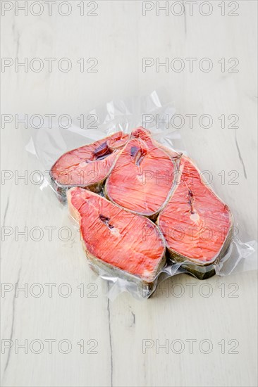 Overhead view of raw salmon steak in vacuum packaging on light background