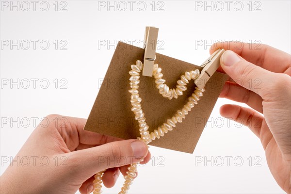 Pearl necklace forms heart shape on paper on white background