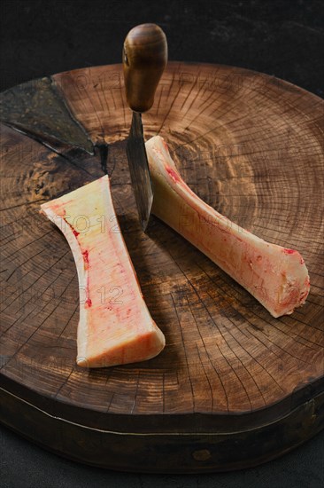 Overhead view of large beef bone marrow chopped with cleaver on half on wooden stump