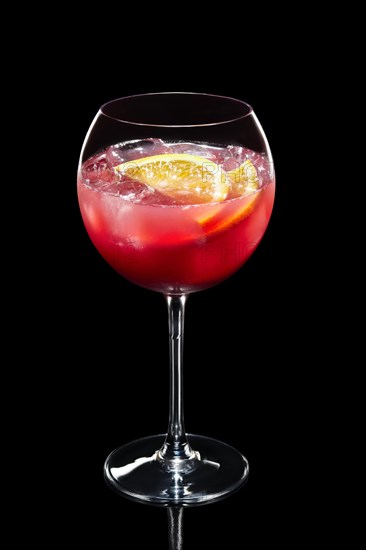Cold lemon cocktail with a sparkling wine and raspberries with ice in wine glass isolated on black