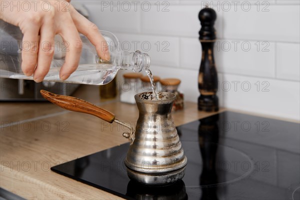 Closeup view of man pouring water into cezve with ground coffee