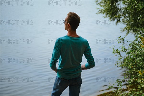 Rear view of a man standing on the shore of a lake and looking at the water