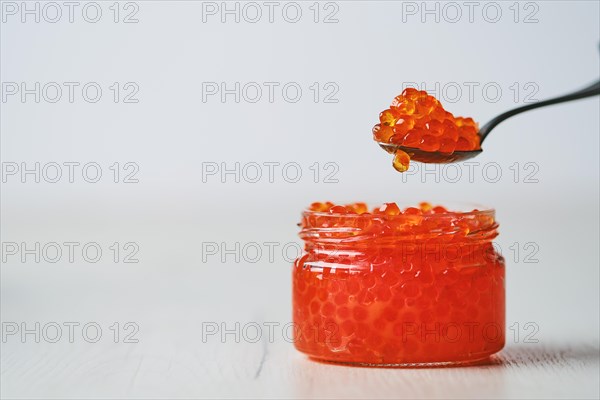 Photo with shallow depth of field of open jar with red caviar and a spoon above it