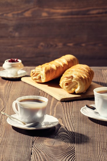 Rolled buns and coffee on wooden table in morning sunlight. Photo with shallow depth of field