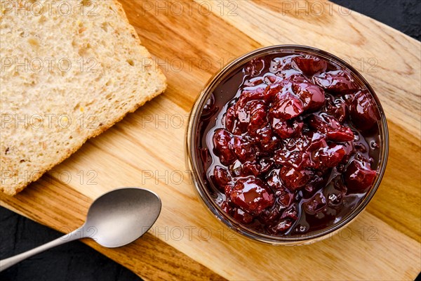 Top view of transparent pot with cherry jam and toast bread