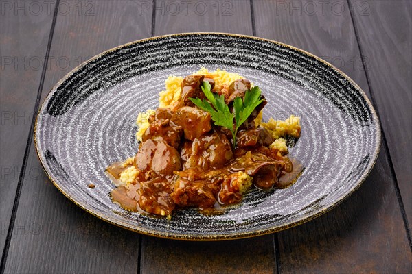 Beef goulash with millet porridge and creamy sauce on dark wooden table