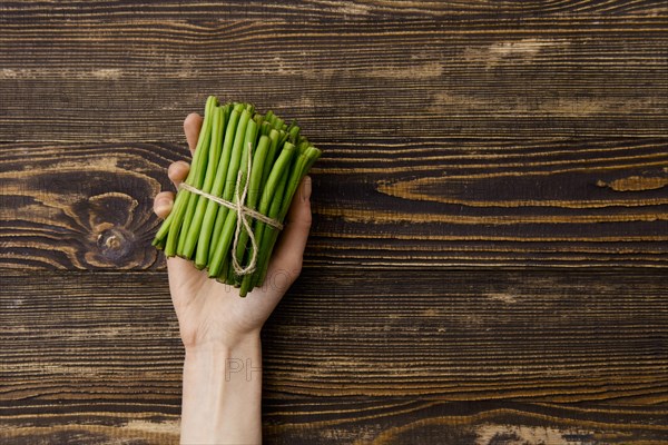 Overhead view of fresh green beans in hand over wooden background