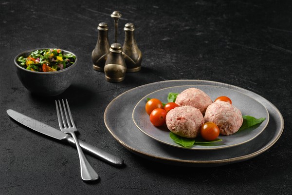 Semifinished frozen veal meatballs on a plate with basil and tomato