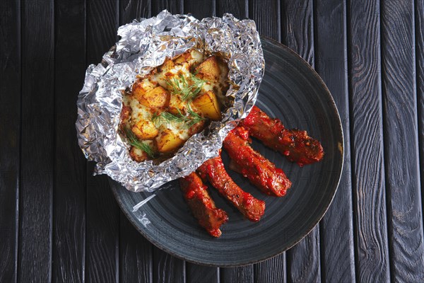 Top view of ried spicy ribs with potato baked with cheese in foil