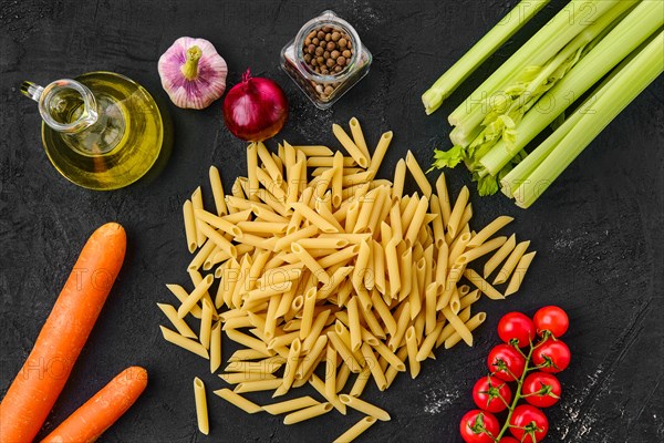 Top view of penne pasta with spice and herbs on black background