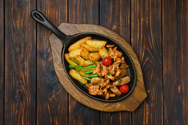 Top view of potato wedges with chanterelles and pork in cast iron skillet