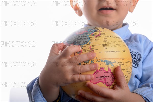 Baby with blue shirt holding a globe in hand on white background