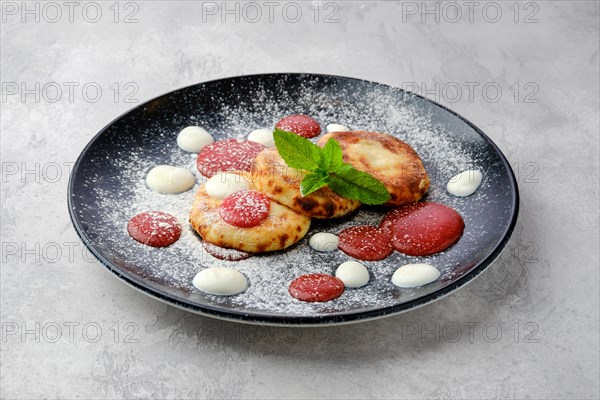 Sweet curd patties with sour cream and strawberry jam on a plate