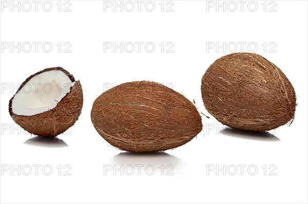 Two whole and one cut half coconuts with shadow on white background